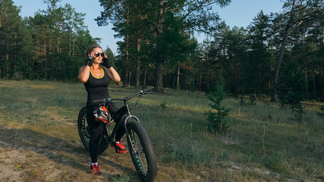 Fat bike also called fatbike or fat-tire bike in summer riding in the forest. Beautiful girl and her bicycle in the forest. She rolls her bike and poses to the operator.