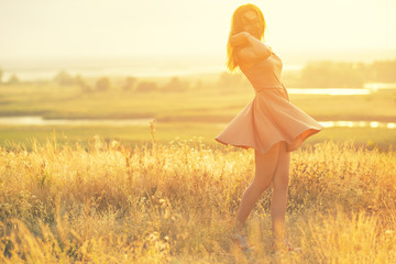 beautiful girl in a field at sunset, a young woman in a haze from the sun enjoying nature