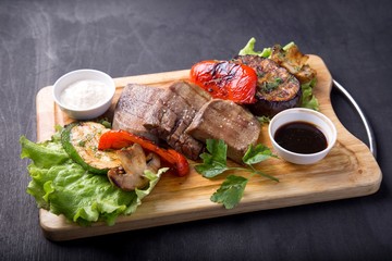Grilled beef tongue served with vegetables and sauce on wooden board