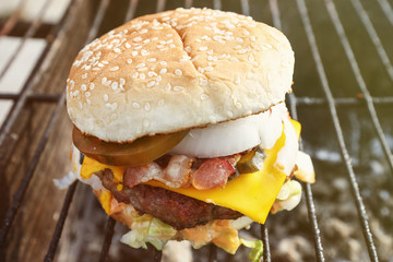 Homemade Burger with meat, bacon, cheese, tomatoes and onions which lies on the grill in the background of nature