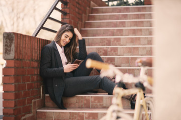 Portrait of woman using smart phone while sitting on stairs outdoors.