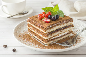Delicious Tiramisu cake with fresh berries and mint on a plate on a light background. Breakfast with a Cup of coffee.