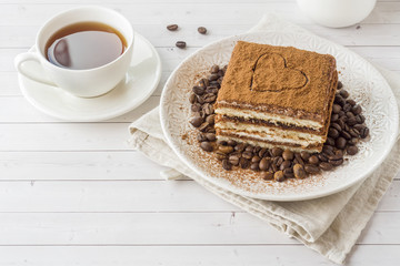 Delicious Tiramisu cake with coffee beans on a plate and a Cup of coffee on a light background