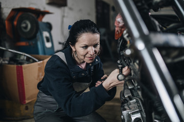 Strong and worthy woman doing hard job in car and motorcycle repair shop.