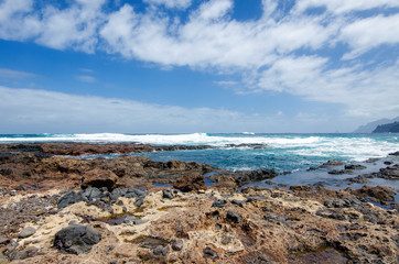 Fototapeta na wymiar Beautiful seascape with view on the Atlantic Ocean, blue sky with white clouds and stone wild beach near Punta del Hidalgo and Anaga Rural Park. Tenerife North. Canary Islands, Spain.