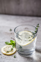 A glittering simple glass on a gray background with water, lemon and thyme