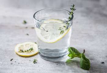 A glittering simple glass on a gray background with water, lemon and thyme