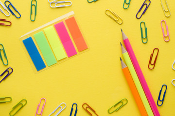 Pencils and colored paper clips on yellow background. Copy space