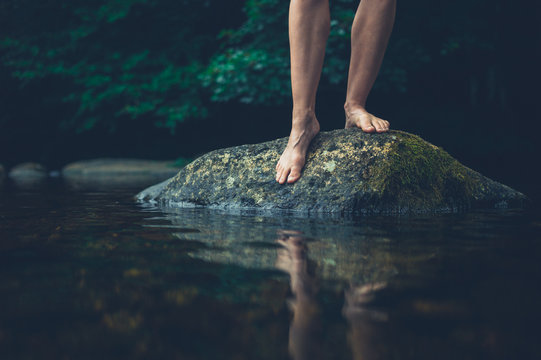 The feet of a young woman on a rock in the river