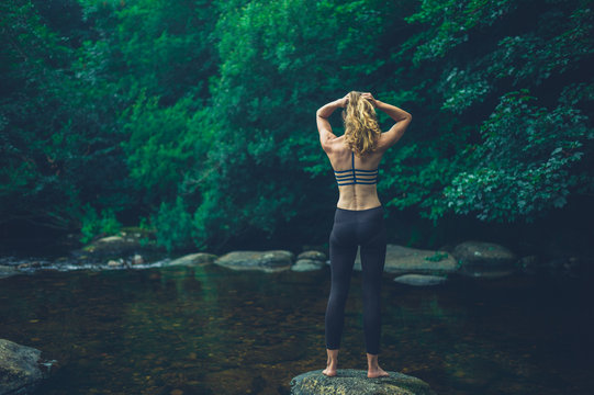 Young fitness woman standing on rock in river