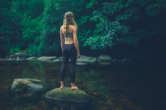 Young fitness woman standing on rock in river