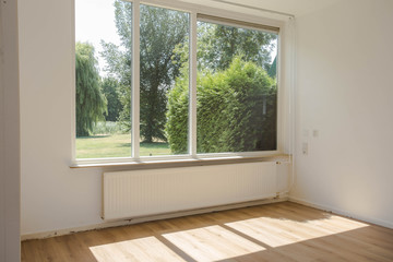 Empty white room with hardwood parquet floor, big window and walls and sunlight from window, With a beautiful green forest nature view