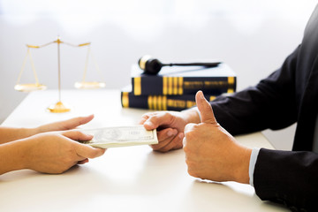 Lawyer being offered receiving money as bribe from client at desk in courtroom.