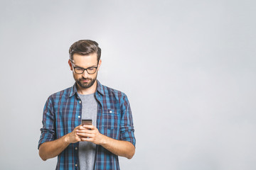Happy young man in glasses typing sms on gray background