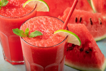 Watermelon slushie with lime, summer refreshing drink in tall glasses on a blue rusty background