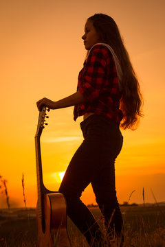 Silhouette of young girl with guitar at sunset