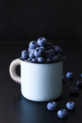 Fresh flavored blueberries in a blue cup on a black background.