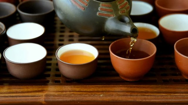 Process of pouring tea into cup from pot at ceremony. Chinese Japanese set on bamboo wooden dripping tray. Freshly brewed beverage. Lifestyle. Wellness balance cultural traditions. Footage
