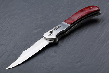 Steel folding knife with an open blade and wooden handle on a stone surface. Steel arms. The concept of weapon, hunting or crime
