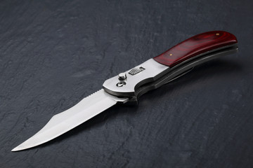 Steel folding knife with an open blade and wooden handle on a stone surface. Steel arms. The concept of weapon, hunting or crime