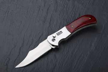 Steel folding knife with an open blade and wooden handle on a stone surface. Steel arms. The concept of weapon, hunting or crime