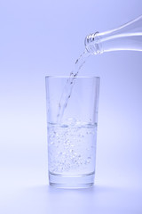 Pouring water into glass from a bottle, on white background