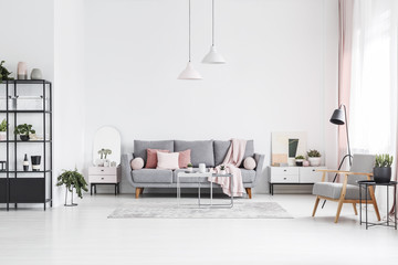 Patterned wooden armchair in white living room interior with pink pillows on grey sofa. Real photo