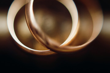 Two golden wedding rings closeup, macro photo of a couple of luxury golden engagement rings on bronze metal background, wedding jewellery