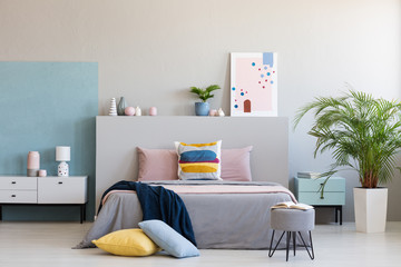 Colorful pillows on grey bed in modern bedroom interior with poster and plants. Real photo - obrazy, fototapety, plakaty