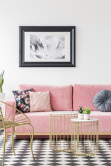 Pink sofa decorated with pillows, painting on the wall and golden tables in a living room interior....