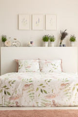 Real photo of floral bedroom interior with a double bed, pillows, plants and paintings
