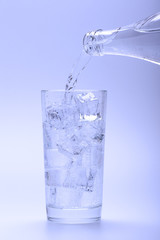 Pouring fresh water into glass with ice from a bottle