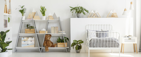 Real photo of a modern kid's room interior with grey shelves, teddy bear, plants, triangles and metal bed - obrazy, fototapety, plakaty