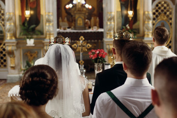 Happy spiritual couple, stylish groom and beautiful brunette bride in white dress holding candles...