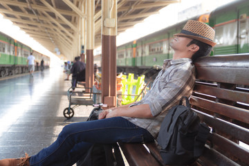 Asian man wearing a hat weave lying on a bench wooden. Waiting for the train at station in the outbound platform.