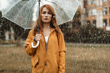 Waist up portrait of unhappy girl holding umbrella in hands. She is looking at camera with...