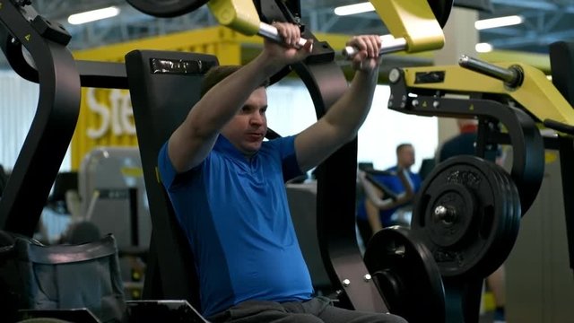 Tilt up of paraplegic man breathing hard and training on chest press machine in gym; wheelchair standing beside him