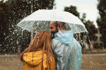 Smiling man walking side by side with woman under umbrella. They are enjoying nature together with content