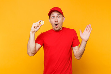 Fototapeta na wymiar Delivery man in red uniform isolated on yellow orange background. Professional shocked male employee in cap, t-shirt courier dealer holding bitcoin, metal golden bit coin. Service concept. Copy space.