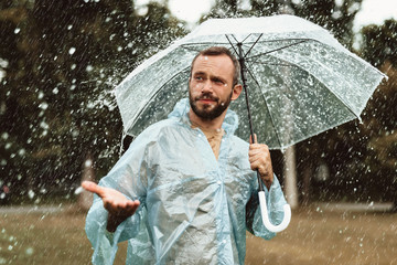 Waist up portrait of satisfied man standing outdoors and holding umbrella. He is stretching hand with delight and looking curious
