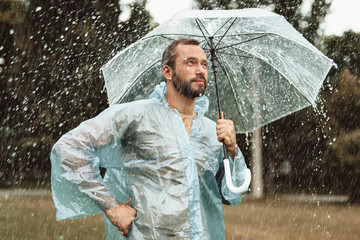 Side view of thoughtful male standing under umbrella. He is contemplating with smile and content...