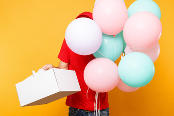 Man giving food order cake box isolated on yellow background. Male employee courier in red cap t-shirt hold colorful air balloons, dessert in empty cardboard box. Delivery service concept. Copy space.