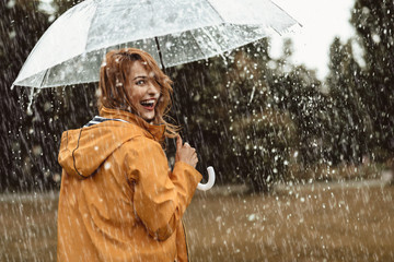 Cheerful pretty girl holding umbrella while strolling outside. She is turning back and looking at camera with true delight and sincere smile. Copy space in right side - obrazy, fototapety, plakaty