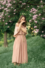 Obraz na płótnie Canvas Young woman in a beautiful dress is standing near a lilac bush