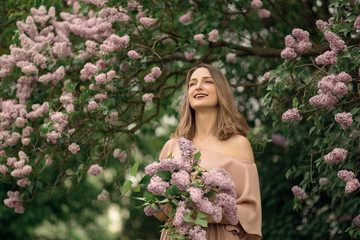 Young woman in a beautiful dress is standing near a lilac bush