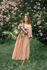 Obraz na płótnie Canvas Young woman in a beautiful dress is standing near a lilac bush