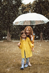 Full length of happy child standing with mother outdoors. Smiling woman is holding umbrella and...