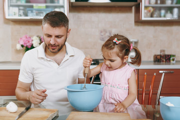 Obraz na płótnie Canvas Little kid girl helps man to cook Christmas ginger cookies, stirs eggs, dough in bowl at table. Happy family dad, child daughter cooking food in weekend. Father's day holiday. Parenthood, childhood.