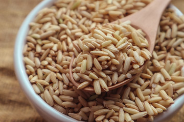 Raw brown rice in a spoon and bowl. top view food background