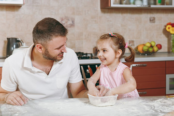 Fototapeta na wymiar Little kid girl play, smearing with flour with man in kitchen at table. Happy family dad, child daughter cooking food, ginger cookies in weekend morning. Father's day holiday. Parenthood, childhood.